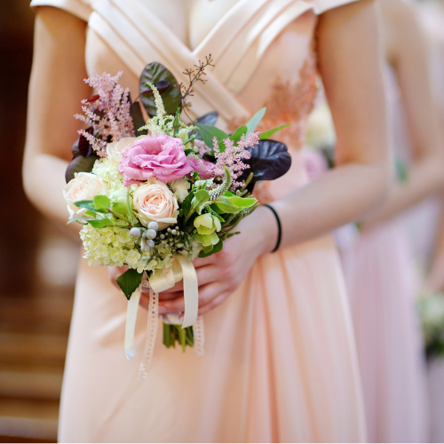 Bridesmaid holding a floral bouquet in a blush dress as part of a coordinated bridal party