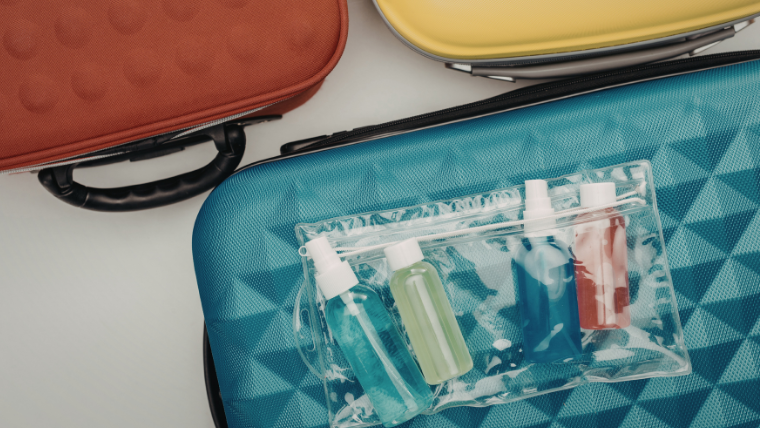 Travel size toiletries in a clear quart-sized TSA bag on top of a teal suitcase