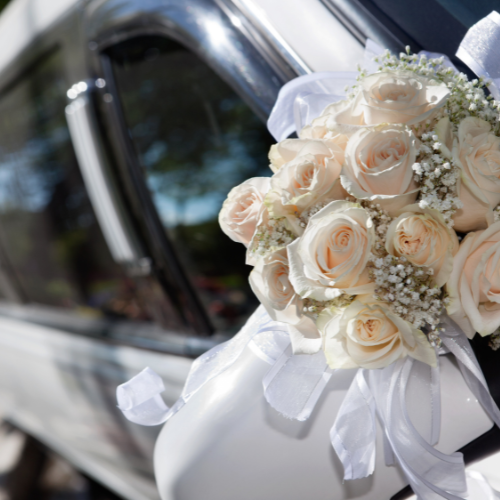 White rose bridal bouquet with ribbon resting on a decorated wedding limousine