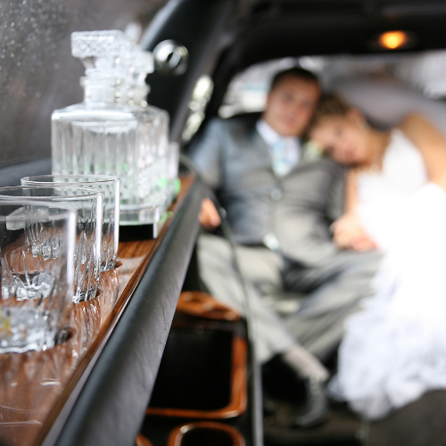 Crystal decanter and glassware inside a luxury wedding limousine with newlyweds relaxing in the background